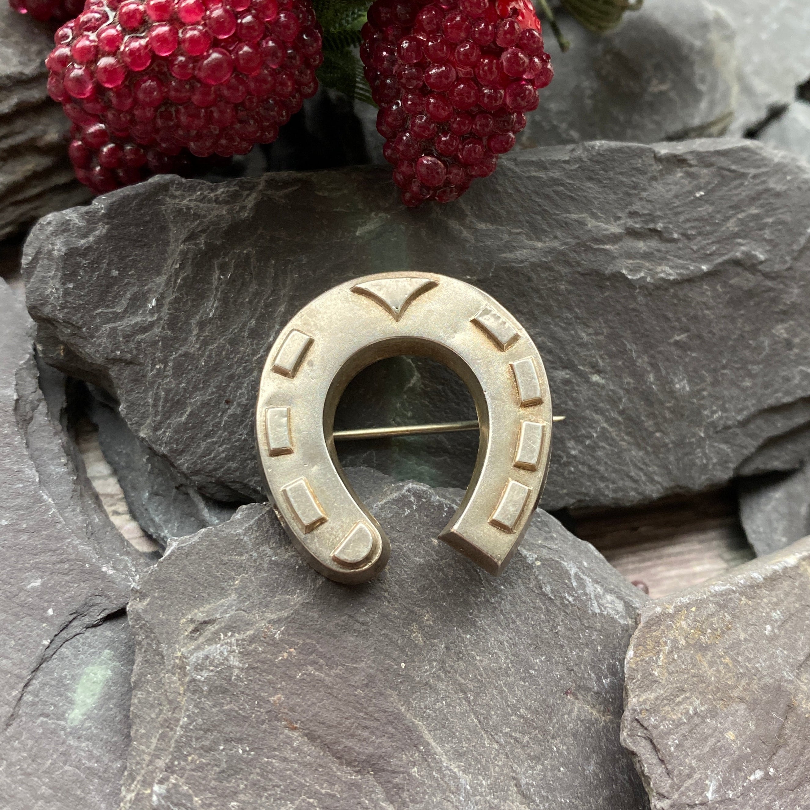 Victorian Silver Horseshoe brooch on a stone surface with red berries in the foreground