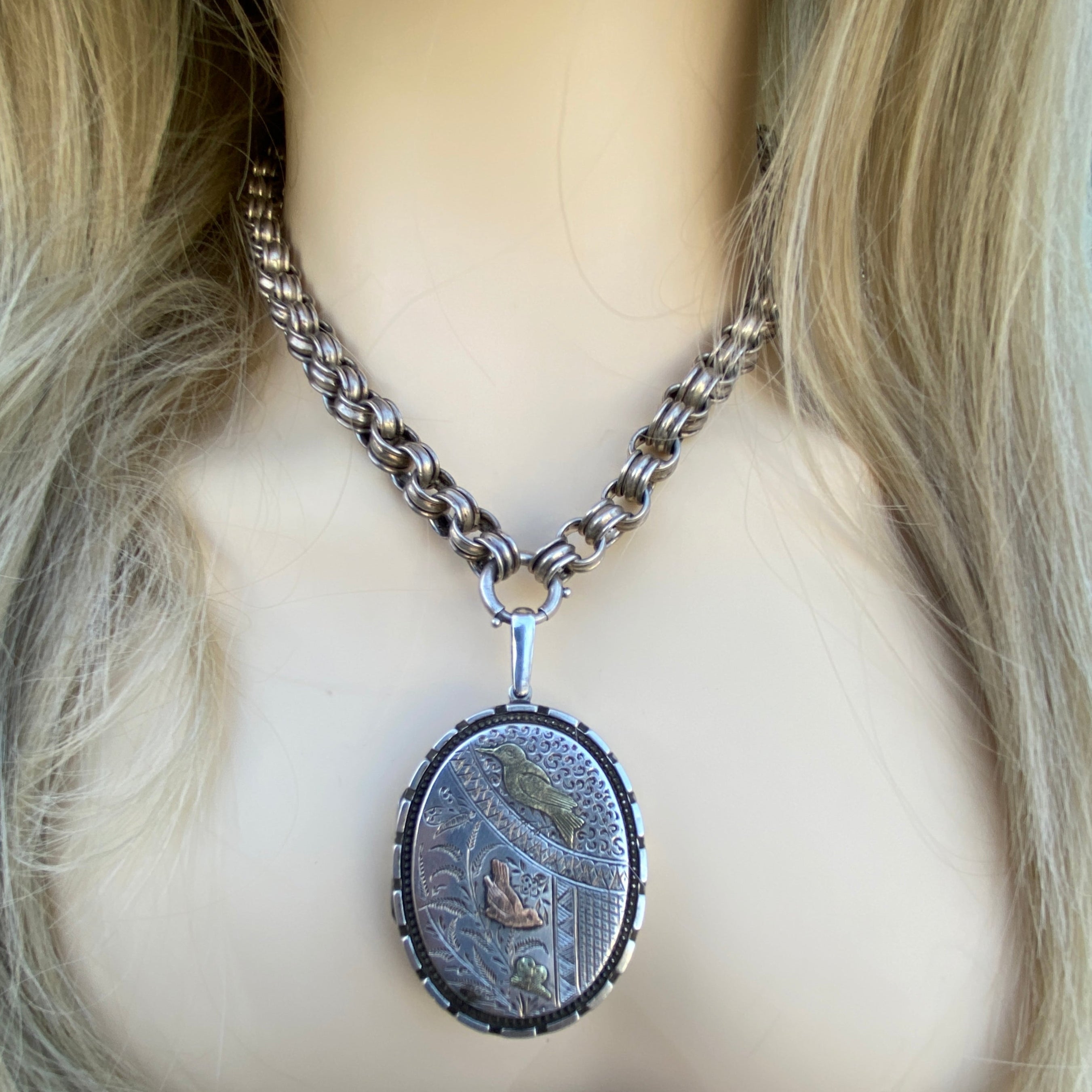 Mannequin head with a silver chain and round decorative piece on a textured surface