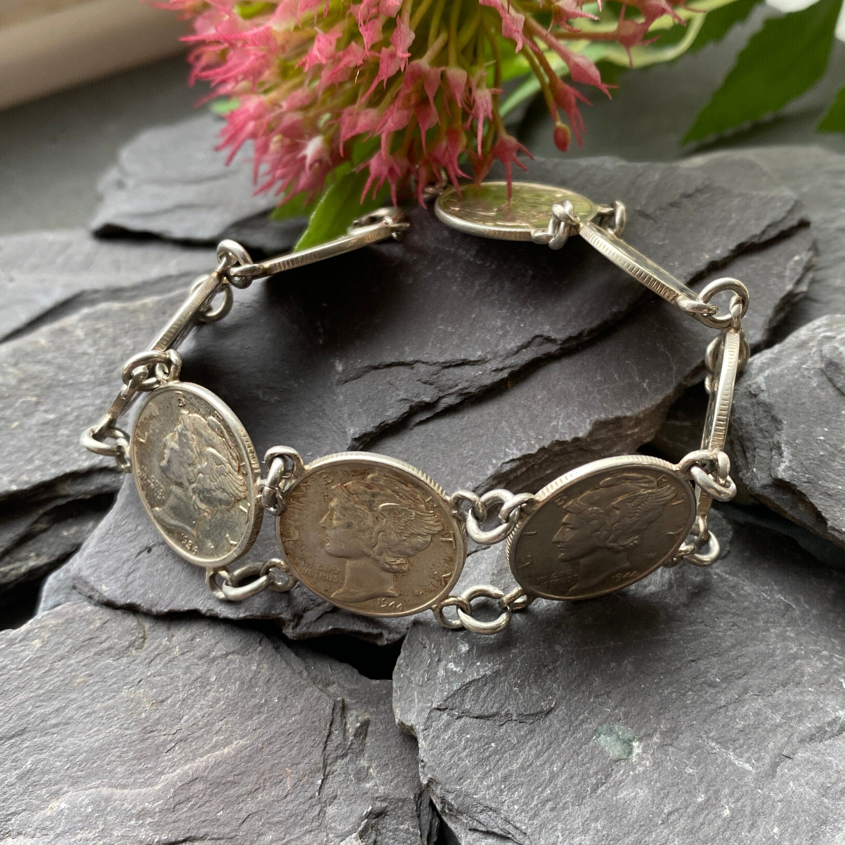 Bracelet with coin charms on a stone surface with pink flowers