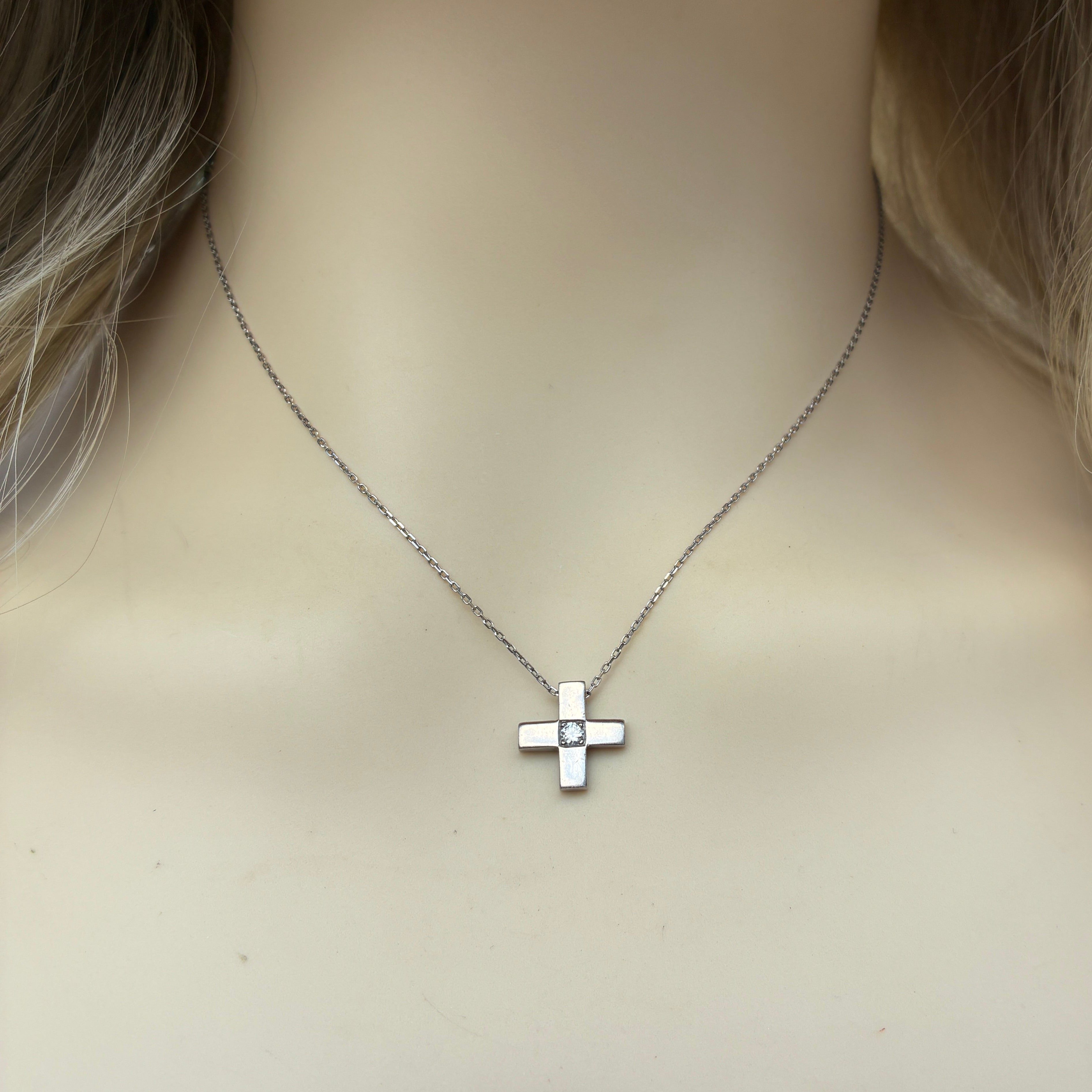 18ct white gold cross or plus sign shaped pendant with central round brilliant cut diamond. Suspended from a 16 inch 18ct white gold chain.