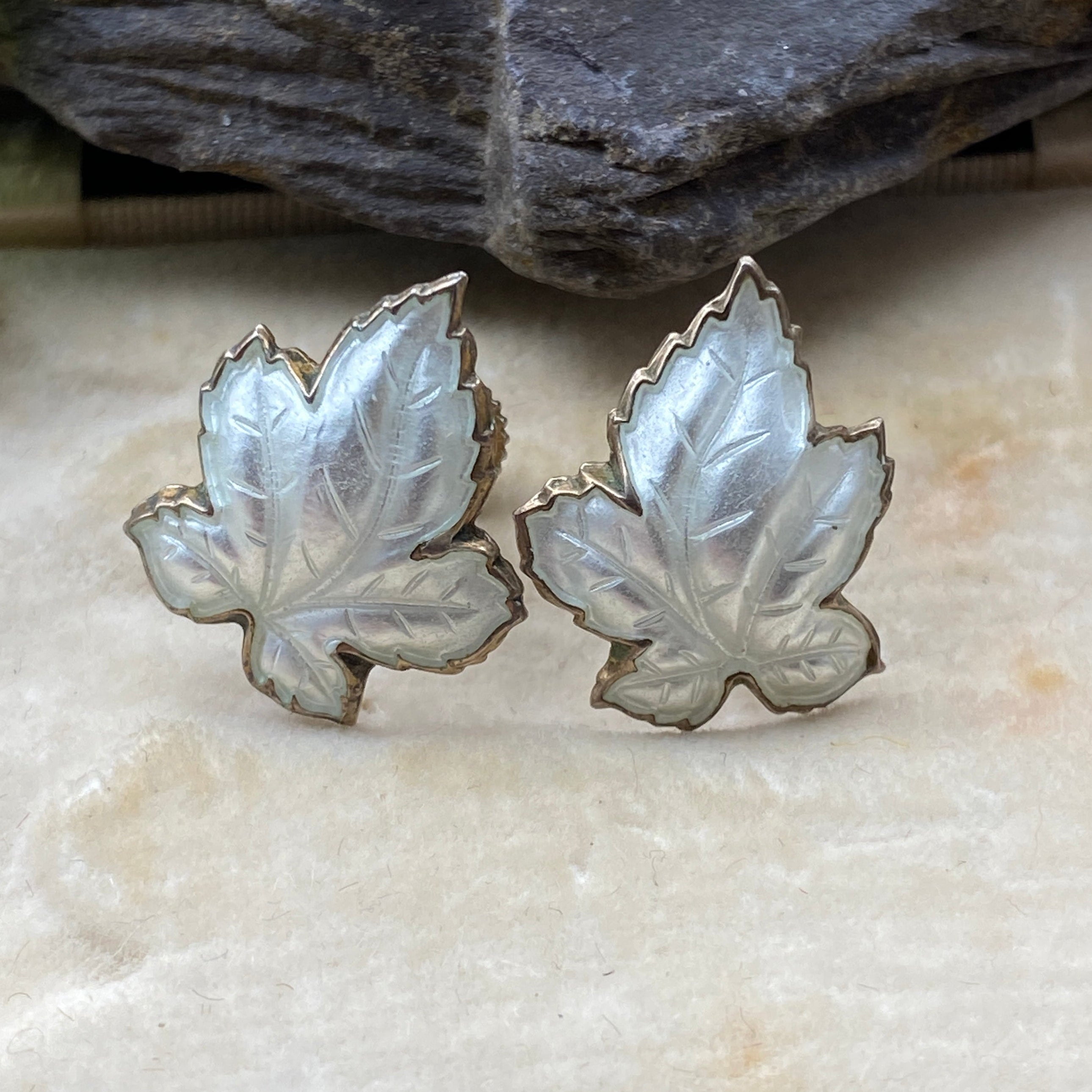 Silver leaf-shaped earrings on a textured stone surface with green leaves in the background