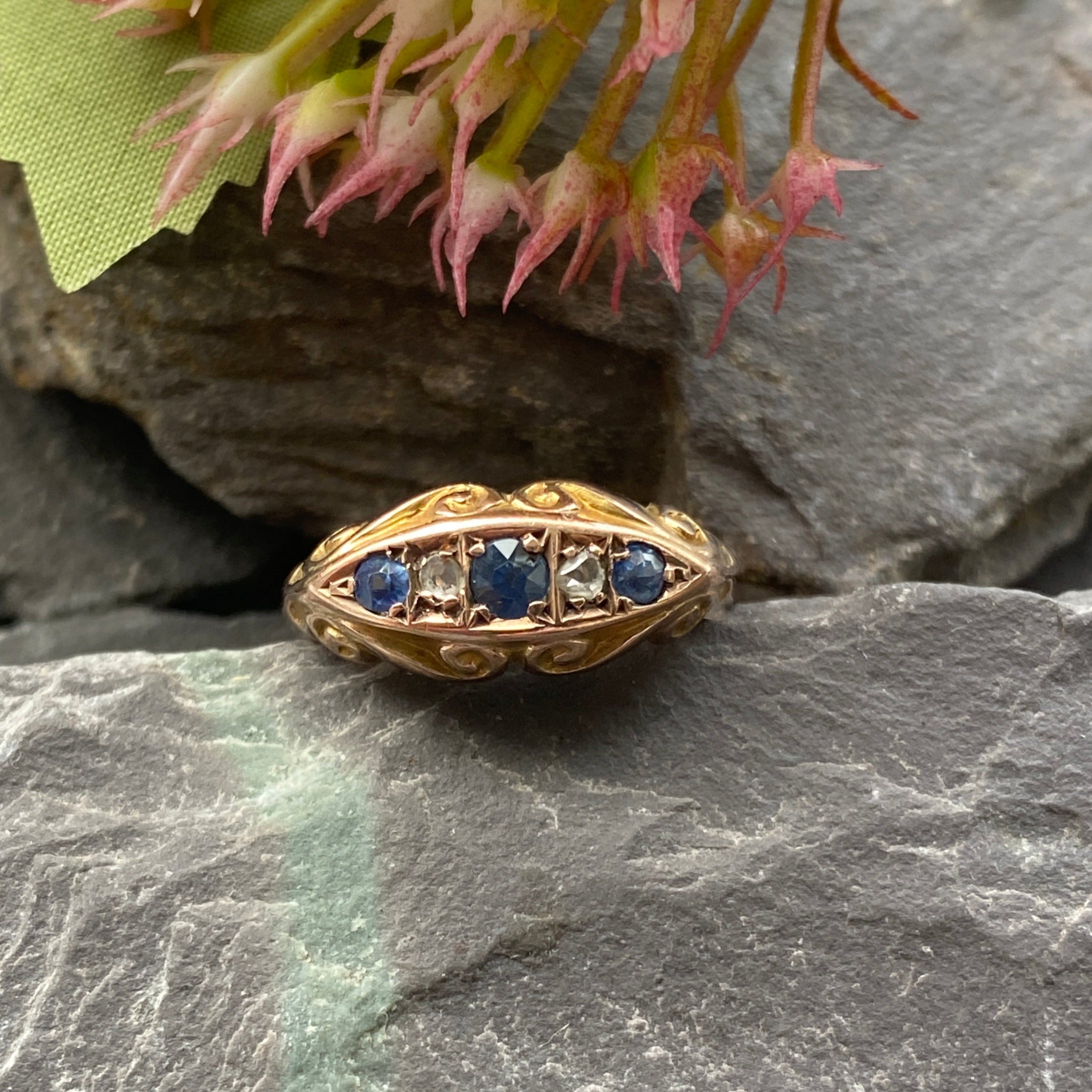 Gold ring with blue stones on a stone surface with pink flowers