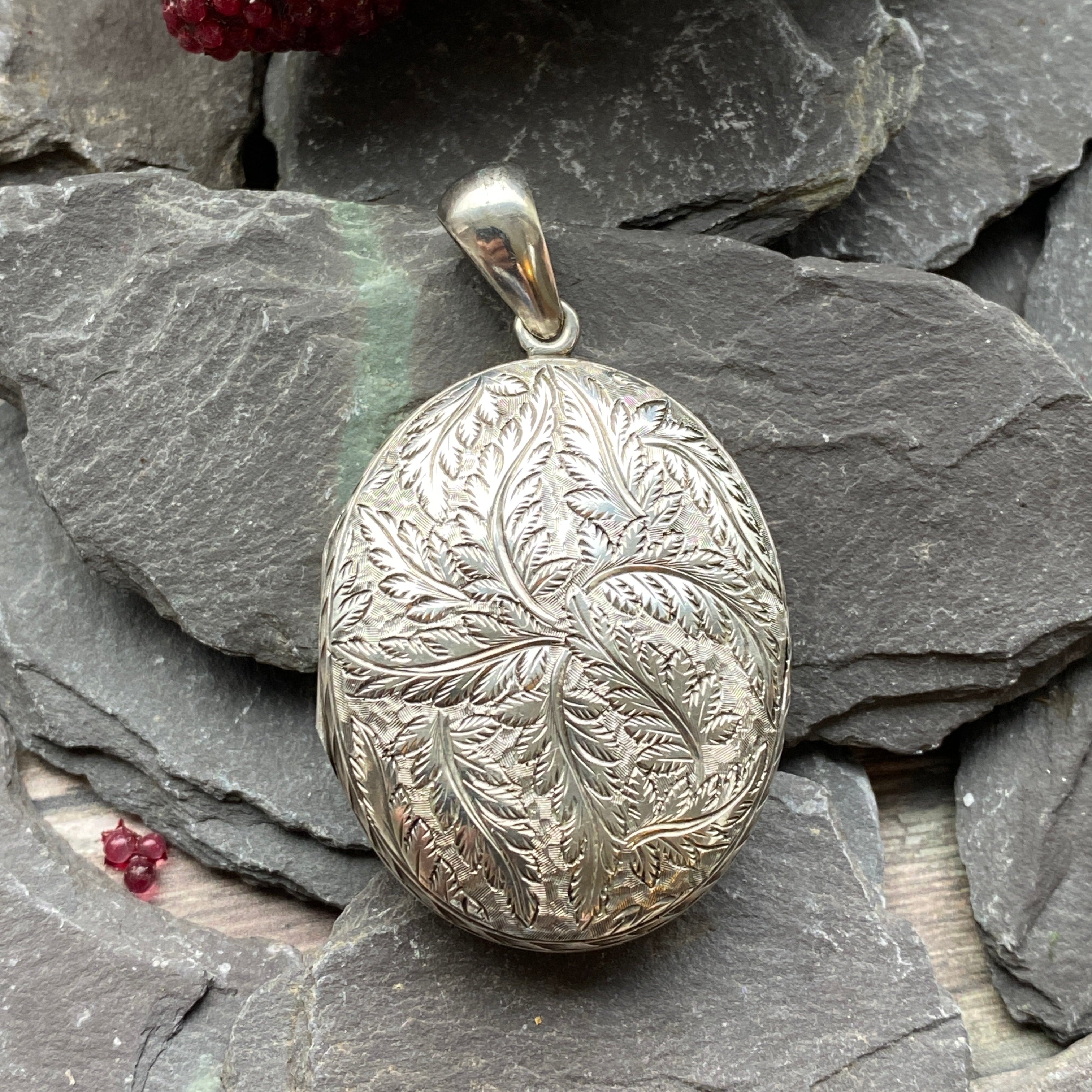 Victorian Silver locket with leaf design on a stone surface with red berries